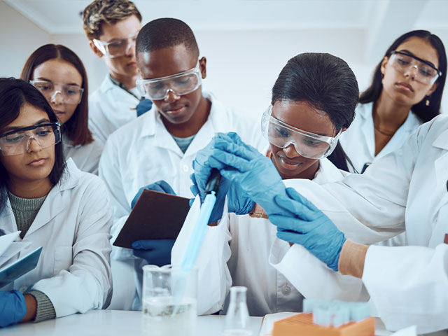 Group of young students learning from science professor